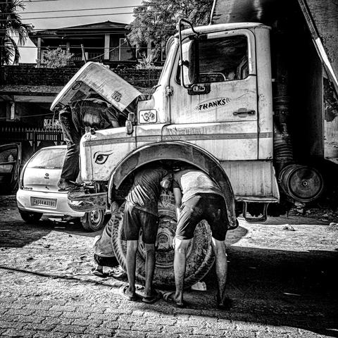 Schwarzweissfotografie von vier Leuten, die an unterschiedlicher Stelle den Kopf in einen Lastwagen stecken. 