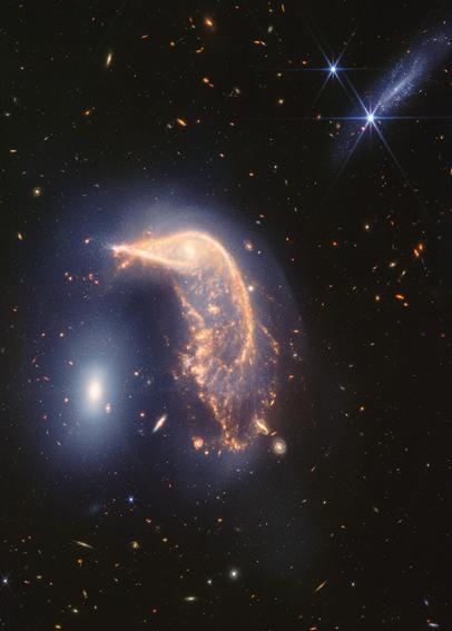 Arp 142, two interacting galaxies, observed in near- and mid-infrared light. At left is NGC 2937, nicknamed the Egg. Its center is brighter and whiter. There are six diffraction spikes atop its gauzy blue layers. At right is NGC 2936, nicknamed the Penguin. Its beak-like region points toward and above the Egg. Where the eye would be is a small, opaque yellow spiral. The Penguin’s distorted arms and orange dust lanes from the bird’s beak, back, and tail. The tail is wide and layered, like a beta fish’s tail. A semi-transparent blue hue traces the Penguin and extends from the galaxy, creating an upside-down U over top of both galaxies. At top right is another galaxy seen from the side, pointing roughly at a 45-degree angle. It is largely light blue. Its length appears approximately as long as the Egg’s height. One foreground star with large, bright blue diffraction spikes appears over top of the galaxy and another near it. The entire black background is filled with tiny, extremely distant galaxies.