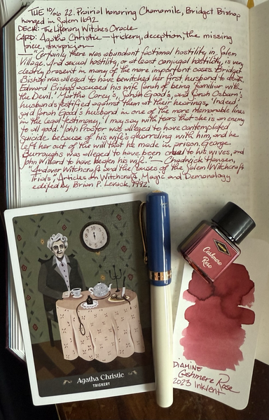 Open notebook with handwritten text from the post at the top of the page with additional text: “Certainly there was abundant factional hostility in Salem Village. And sexual hostility, or at least conjugal hostility, is very clearly present in many of the more important cases. Bridget Bishop was alleged to have bewitched her first husband to death. Edward Bishop accused his wife Sarah of being ‘familiar with the Devil.’ Martha Corey’s, Sarah Good’s, and Sarah Osburn’s husbands testified against them at their hearings. ‘Indeed,’ said Sarah Good’s husband, in one of the more memorable lines in the legal testimony, ‘I may say with tears that she is an enemy to all good.’ John Procter was alleged to have contemplated suicide because of his wife’s quarreling with him, and he left her out of the will that he made in prison. George Burroughs was alleged to have been cruel to his wives, and John Willard to have beaten his wife.” — Chadwick Hansen, “Andover Witchcraft and the Causes of the Salem Witchcraft Trials,” Articles on Witchcraft , Magic and Demonology edited by Brian P. Levack, 1992. Below the text is a card with a folk art style image of Christie sitting at a table with a pot and cup of tea, a noose, a bun with a knife stuck in dripping blood and a clock on the wall behind her that only goes to 10. Next to the card is a blue and white fountain pen with gold tone trim and a swatch of dusty rose ink under a small square bottle containing said ink. 