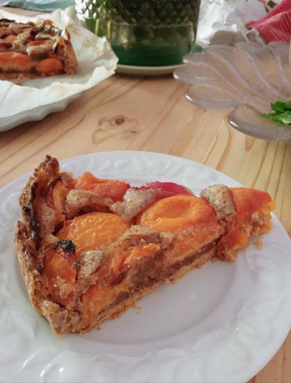 Slice of peach and almond torte on a white porcelain plate on a wooden table.