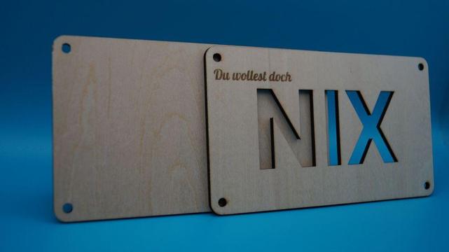 Zwei Holzplatten mit ausgelasertem Schriftzug „Du wolltest doch NIX“, dahinter ein Geldschein. Die humorvolle Geschenkverpackung spielt mit dem Wunsch „Ich will nichts“.