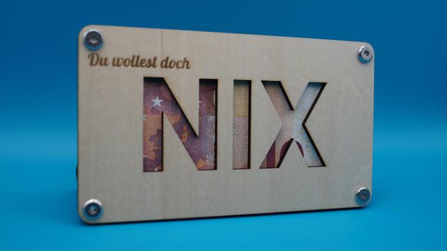 Zwei Holzplatten mit ausgelasertem Schriftzug „Du wolltest doch NIX“, dahinter ein Geldschein. Die humorvolle Geschenkverpackung spielt mit dem Wunsch „Ich will nichts“.