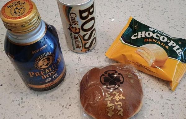 Two canned coffees and two snacks. The snacks are a banana filled cake disk, and a pancake-and-red-bean item called a dorayaki.