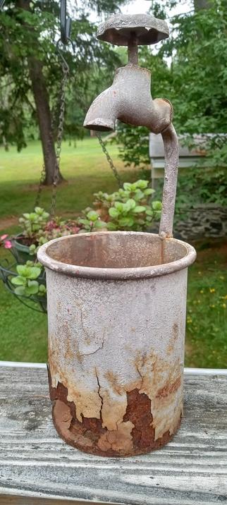 A metal planter with a water spigot welder to the top. The bottom of the planter is rusted through. 