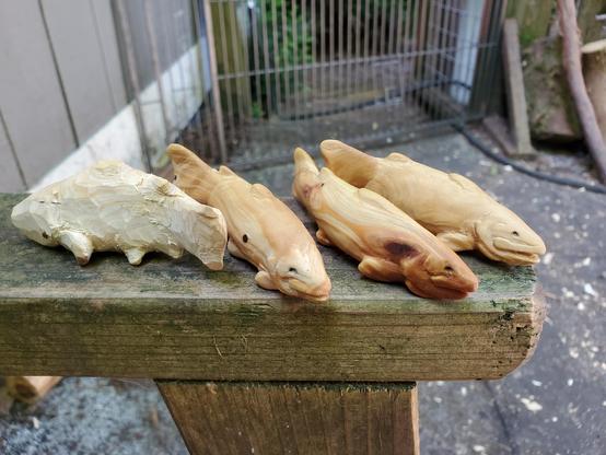 four small carved trouts made of redwood. three are finished and oiled; one is still rough and needs to be sanded and detailed