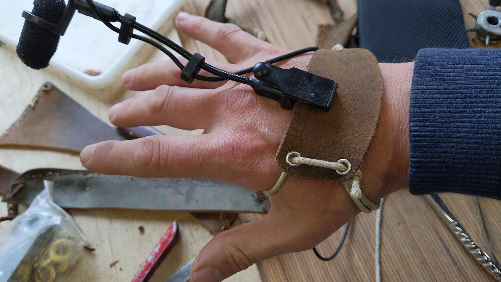On voit une gaine constituée de deux pièces de cuir qui fixent un micro sur le dos de la main.