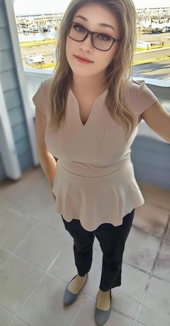 Stellar standing on a balcony in front of the marina, wearing glasses, a light color peplum top, black pants, and gray flats, presenting a casual "ready-for-the-day" look.