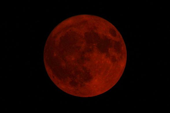 Photograph of a full moon colored red by wildfire smoke.