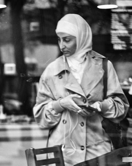 Black and white photo of a woman wearing a head covering while holding a mobile phone.