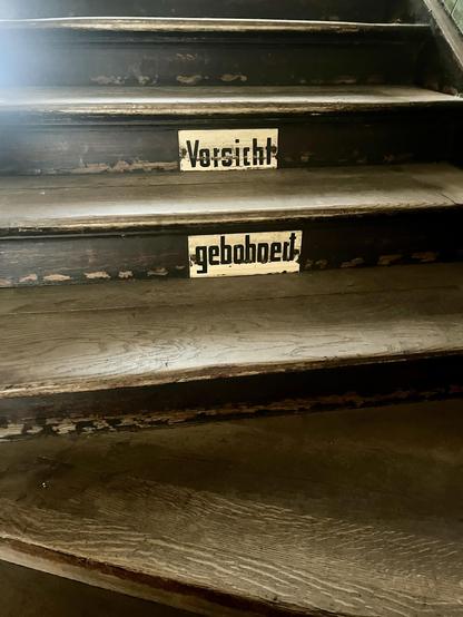 Dunkle Treppenstufen aus Holz. An zwei Stufen das Emailleschild mit der Aufschrift Vorsicht gebohnert.