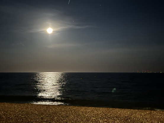 Moon over the calm waters of the British Channel. At the horizon one can see some red lights of an off shore wind park.