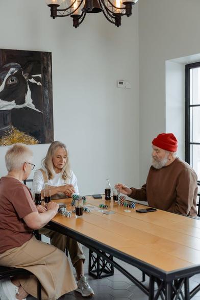 Three people engaged in a card game around a table, focused on their hands and the cards laid out before them