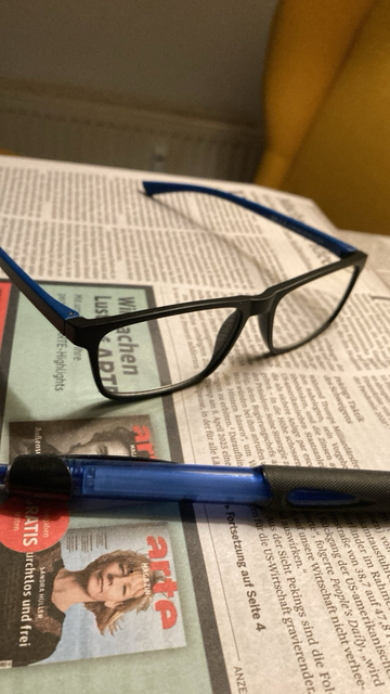 Brille liegt neben einem Stift auf einer Zeitung