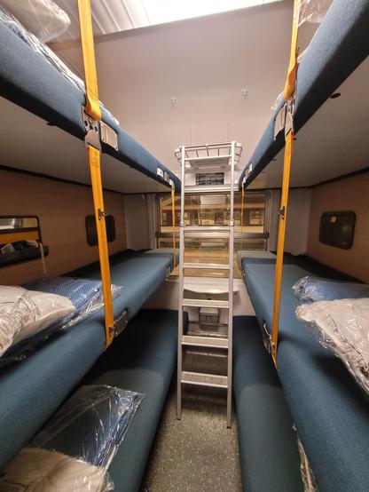 6-bed couchette compartment: triple bunk-bed on each side, facing a metal ladder in front of the window. Blue beds attached by yellow seat belts, pillows and blankets in plastic packaging.