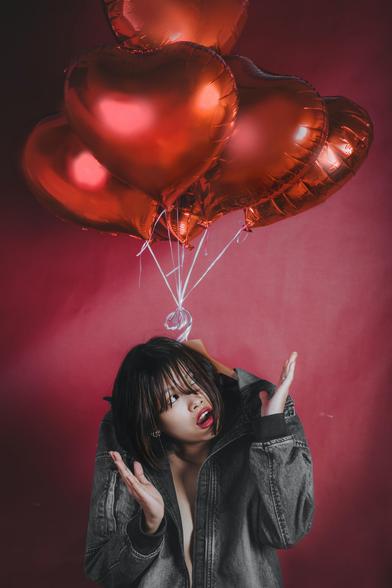 Young woman getting pulled up at the back of her shirt by heart balloons.
