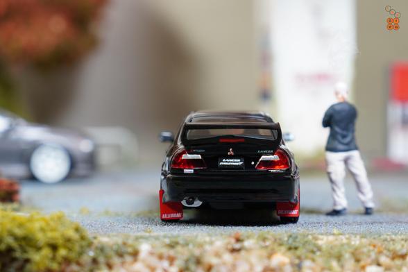 A rear side of Mitsubishi Lancer GSR Evolution V 1998 with Mud Flap, Pyrenees Black by Hobby Japan in 1:64 scale with 1:64 figure on AREA 164