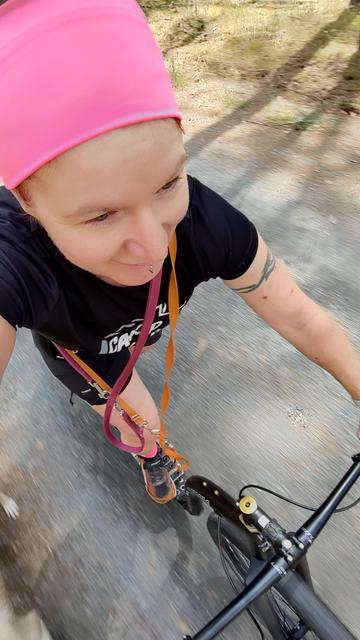 Ein Selfie beim Scooter-Training. Ich stehe mit einem Bein auf dem Trittbrett des Rollers, das andere ist nicht sichtbar, es kickt gerade nach hinten. Man sieht den Lenker, einen Arm und meinen Kopf samt pink-farbenem Stirnband.