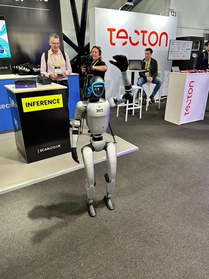 The pictures shows a robot controlled by an attendee at the AI Summit event in front of a sponsor booth.