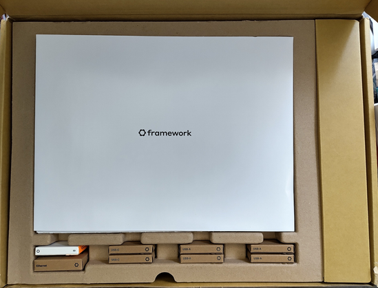 **TL;DR:** This is an unboxing of a Framework Laptop with various modular ports including USB-A, USB-C, Ethernet, and storage expansion.

**Text Extracted:**

* framework
* USB-C
* USB-C
* USB-A
* USB-A
* USB-A
* Ethernet
* 250

**Image Description:**
The image shows the inside of a cardboard box containing a Framework Laptop and its modular expansion cards. The top center contains a white envelope or document labeled “framework.” Below it, neatly slotted in cardboard compartments, are labeled modules: two USB-C ports, three USB-A ports, an Ethernet port, and a storage expansion module labeled "250". The box design is eco-friendly with minimalist packaging, emphasizing the modular and customizable nature of the Framework Laptop.
