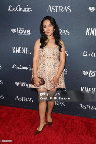Arun Storrs smiling on the red carpet of the Astra TV Awards. She wears a mini-dress in gold patterned fabric.
