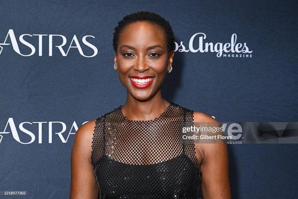 Tracy Ifeachor smiling on the red carpet of the Astra TV Awards. She wears a black form-fitting net dress without sleeves + a strong red lip.