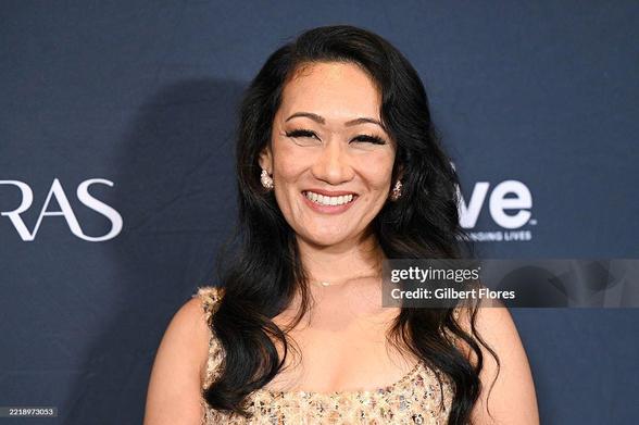 Arun Storrs smiling on the red carpet of the Astra TV Awards. She wears a mini-dress in gold patterned fabric.