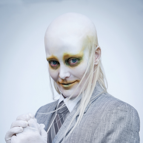 Karin Dreijer looking about as creepy as possible... with bald head, stringy hair on the sides, gray suit and tie, and white rubber gloves