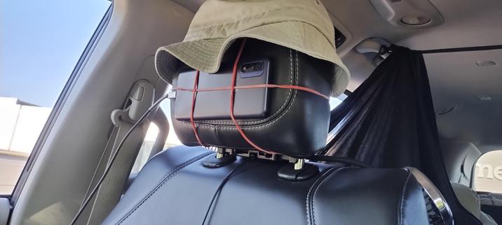 Photo of my old android phone wired up as a makeshift security camera, attached to the headrest of the passenger seat held in place by rubber bands. Also he is wearing a hat :)