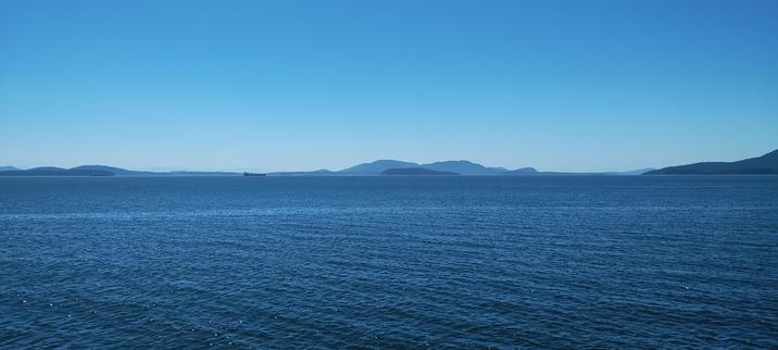 Photo of Larrabee State Park overlooking the bay, just serene waters and clear blue skies for miles; a cargo ship can be seen in the distance.