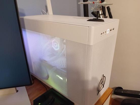 The PC, now assembled and on my desk. It is a white case and some RGB can be seen shining through the side mesh panel.