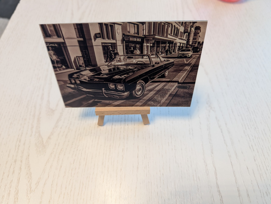 A black and white photo of a classic car on an aluminium plate, sitting on a tiny picture stand.