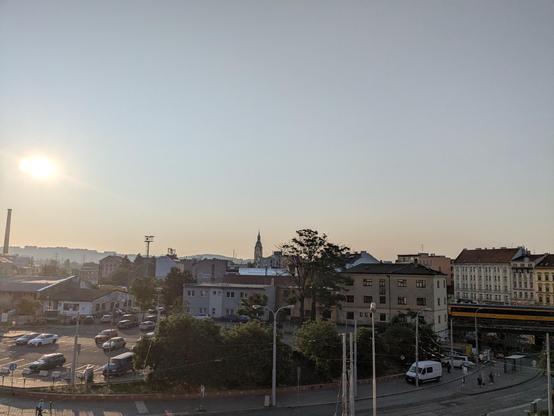 City skyline of Brno, street in the front, sunrise in the back, many buildings and cars. 