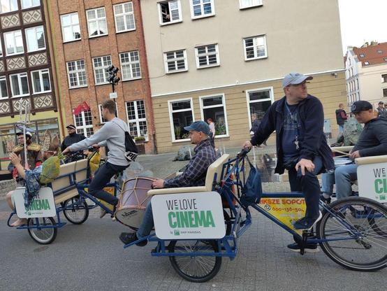 People on bike rikshas with a large sign sign: We love cinema