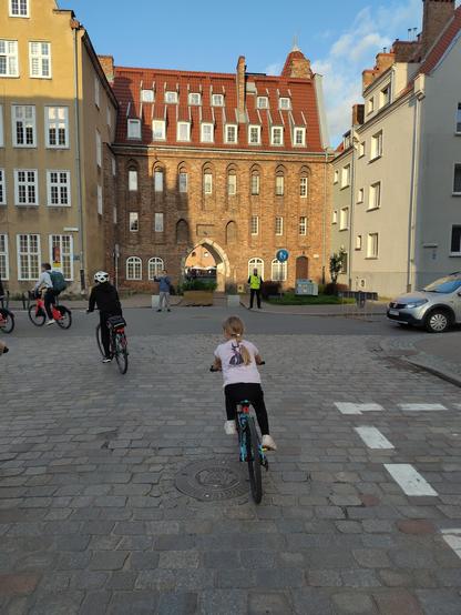A girl cycling on coblestones next to old buildings