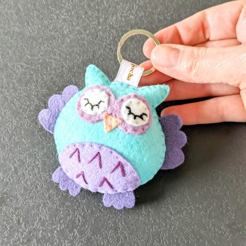 Main qui tient un Porte-clés chouette hibou turquoise et mauve par l'Atelier Jocha.