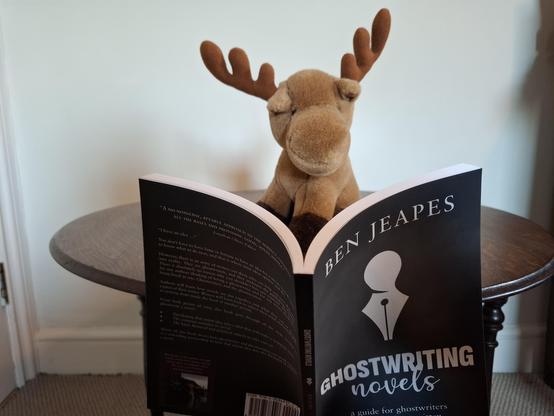 Photo shows cuddly elk reading a book.