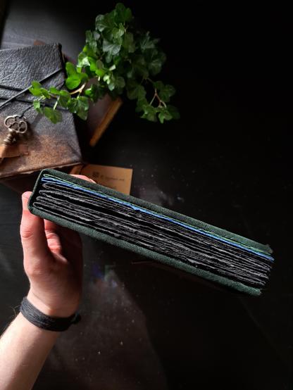 The handmade book photographed from above with its pages pressed shut. Most of the pages are thick black paper with a couple blue and green pages in the end.