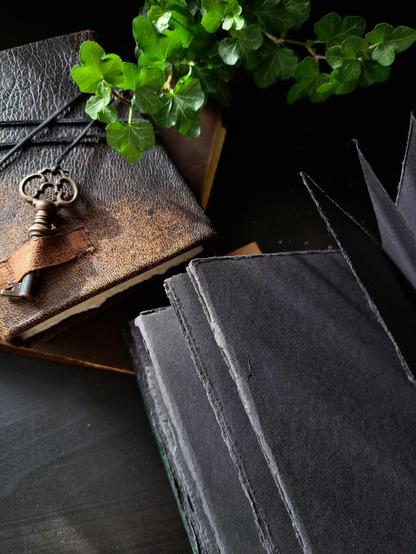 A close up of the black hand torn pages with another handmade leather sketchbook with a key in the background.