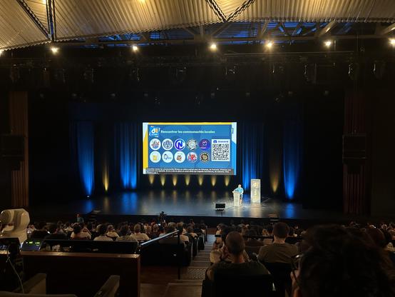 Salle comble du DevLille durant la Keynote d'ouverture. Écran pour présenter les nombreuses communautés et leur stand sur les deux prochains jours. 