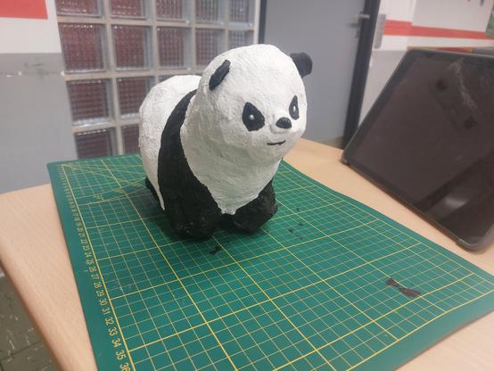 Eine Pandafigur aus Pappmaschee auf einer grünen Matte