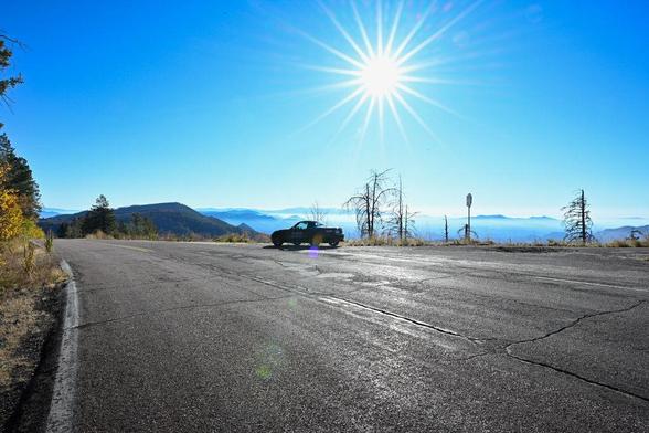 A black Mazda Miata parked on a mountain road at sunrise in Arizona. Bright sunbeams cut through the morning sky, with soft layers of mountains visible in the distance.