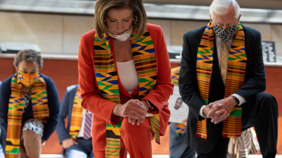 Nancy Pelosi and other Democrats Neil on one knee wearing Kente cloth. 