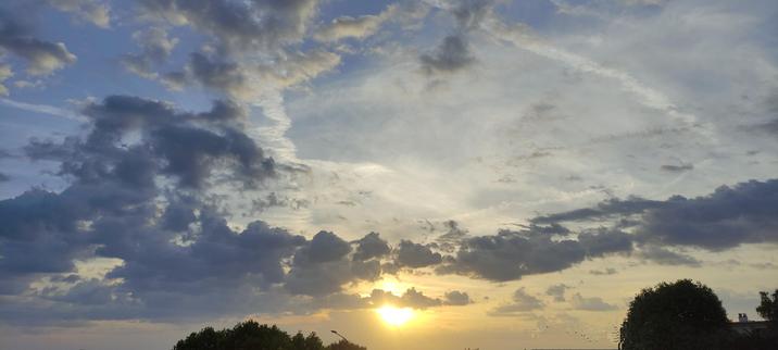 Lever de soleil perçant sous un ciel nuageux, entre bleu profond et doré doux, avec les arbres sombres à l’horizon, comme en silence face à la lumière qui monte