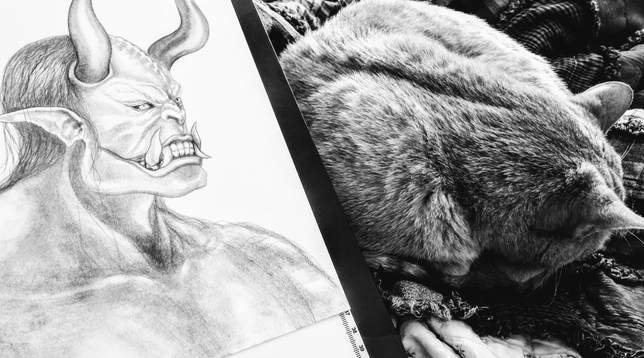 Black and white photo of a caramel tabby cat curled up next to a Oni sketch by Konaa mac Nessa