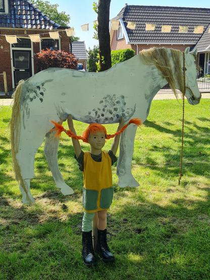 Pop verkleed als Pippi, met armen omhoog onder een wit paard dat ze optilt.