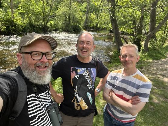 A selfie of three men in their fifties, who despite appearances, are actually all brothers. They are standing in front of the fast moving River Dove in Dove Dale.