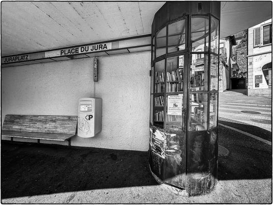 Schwarzweissfotografie mit Bücherkabine an einer Bushaltestelle.