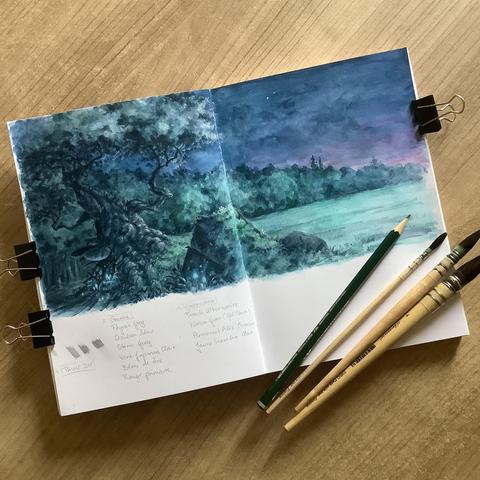 A photo of an open sketchbook placed on a wooden desk and held open with bull clips. Three brushes and a pencil are placed on one corner of the sketchbook. The pages feature a twilight landscape of a treeline behind an open field spanning both pages. A gnarled tree stands on the left in the foreground, surrounded by overgrown chunks of stone ruins. Little glowing blue mushrooms grow around the trees and ruins.
Beneath the landscape notes of colours written in graphite are visible.