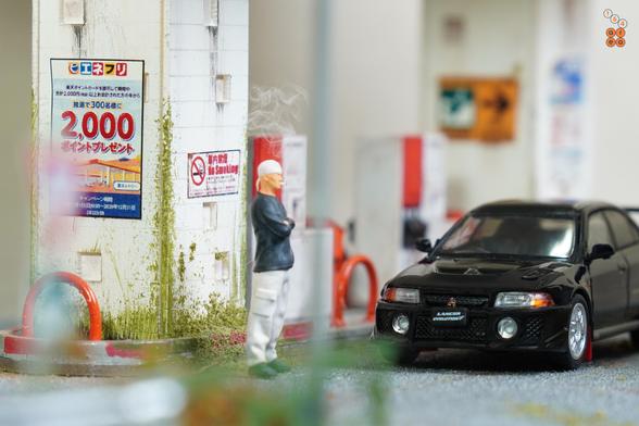 A Mitsubishi Lancer GSR Evolution V 1998 with Mud Flap, Pyrenees Black by Hobby Japan in 1:64 scale with 1:64 figure on AREA 164