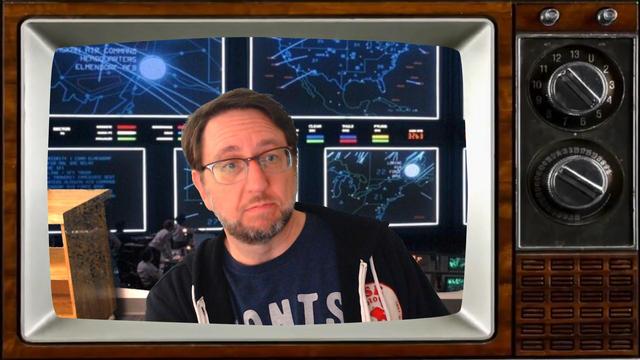 A guy stuck in a TV while a still from War Games is in the background. 